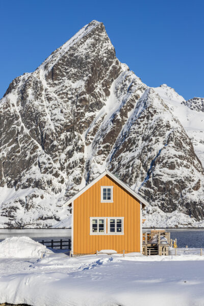 Malerisch gelegenes Haus im Fischerdorf Sakrisøy mit dem Berg Olstind (675 m) im Hintergrund. Das Dorf liegt am Reinefjord zwischen Reine und Hamnøy in der Gemeinde Moskenes im Lofoten-Archipel, Norwegen, Fylke Nordland